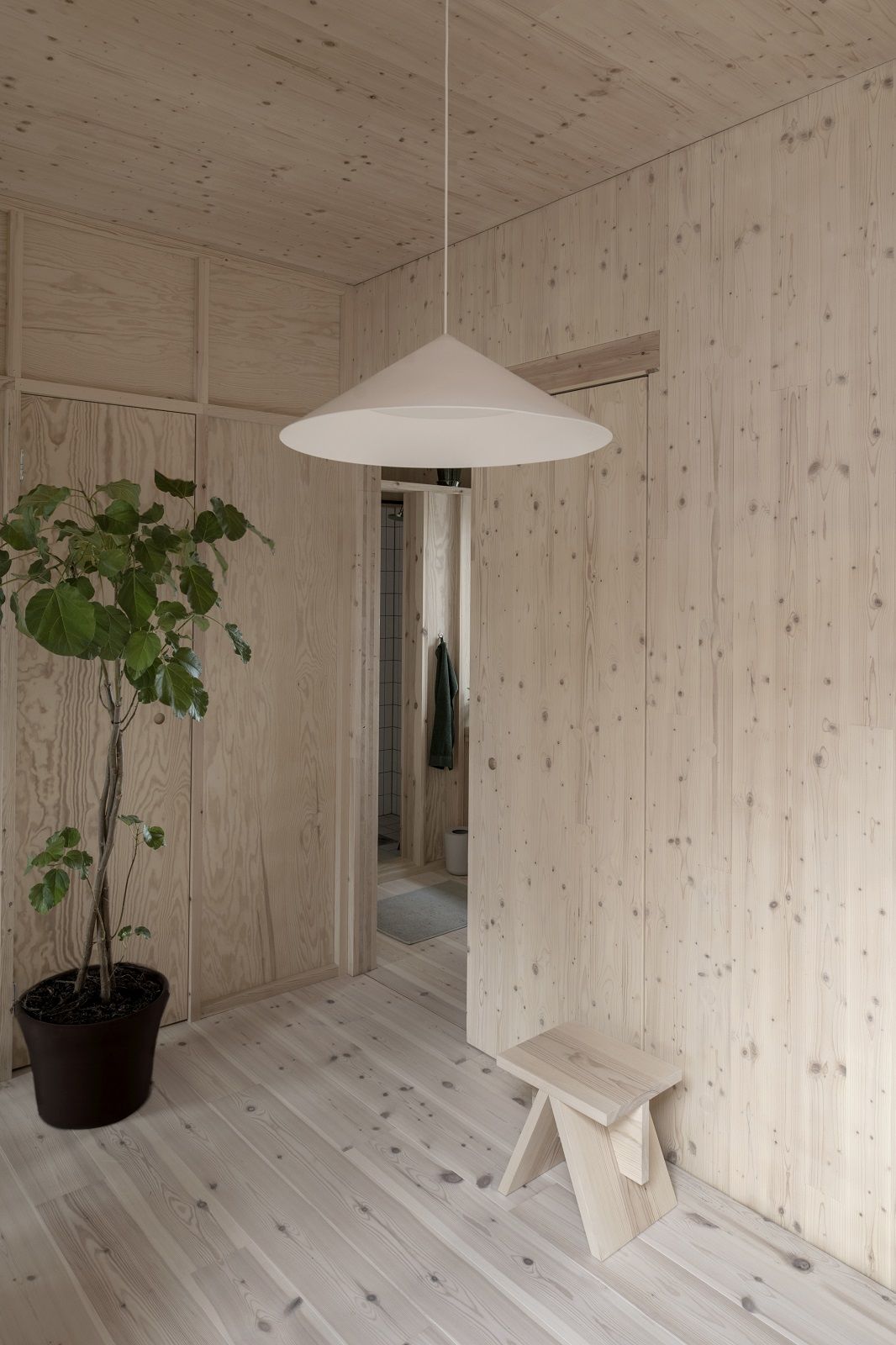 Helle w221 S3 Medium Pendelleuchte von wästberg in einem modern holzvertäfelten Raum mit Pflanze.