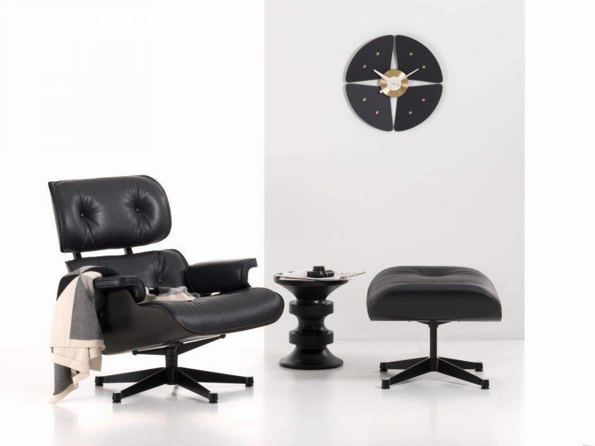 Schwarze Petal Clock Wanduhr von Vitra über einem schwarzen Sessel mit Hocker und Beistelltisch.