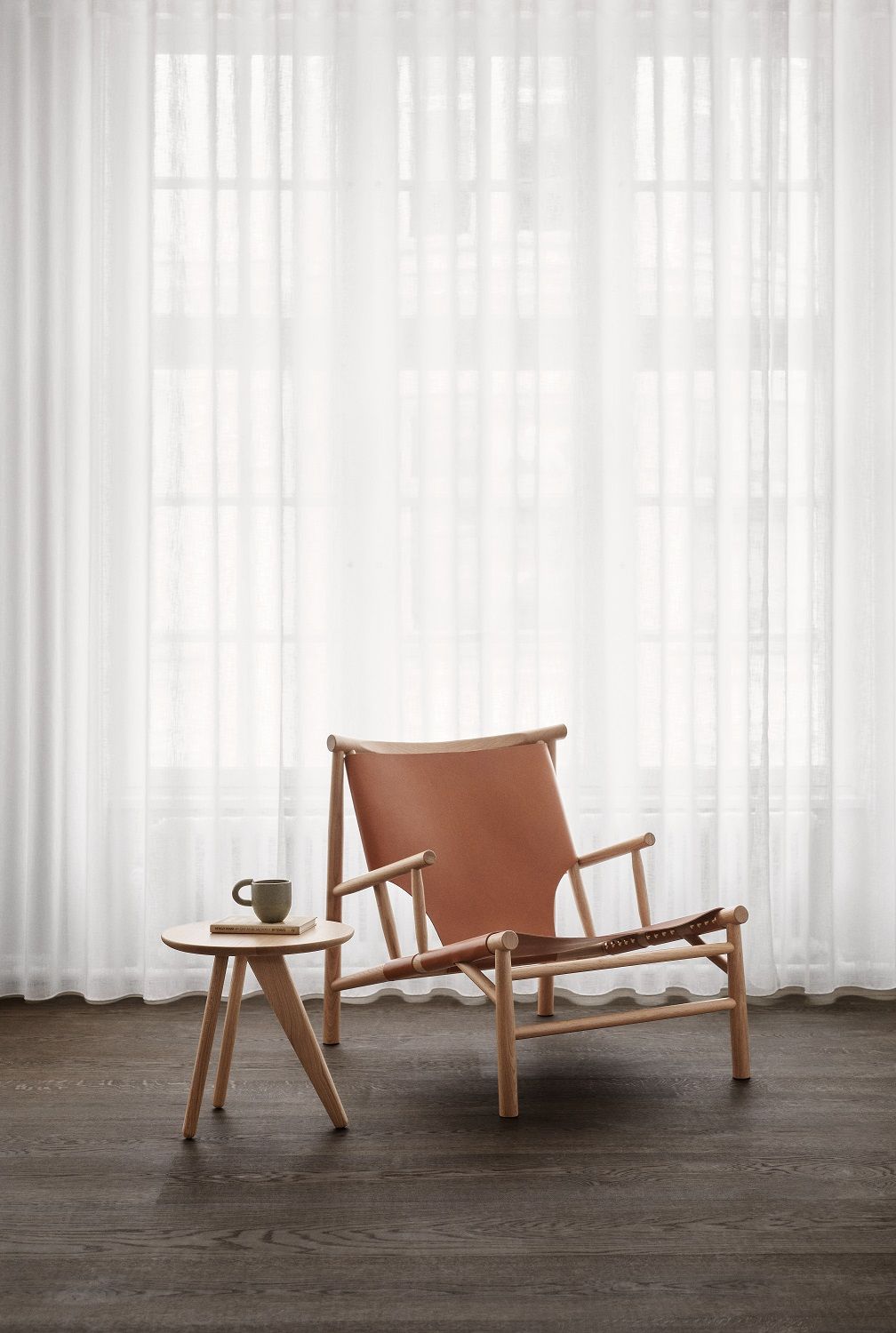 Norr11 Fin Side Table Beistelltisch aus Eichenholz neben einem Ledersessel mit Tasse und Buch.