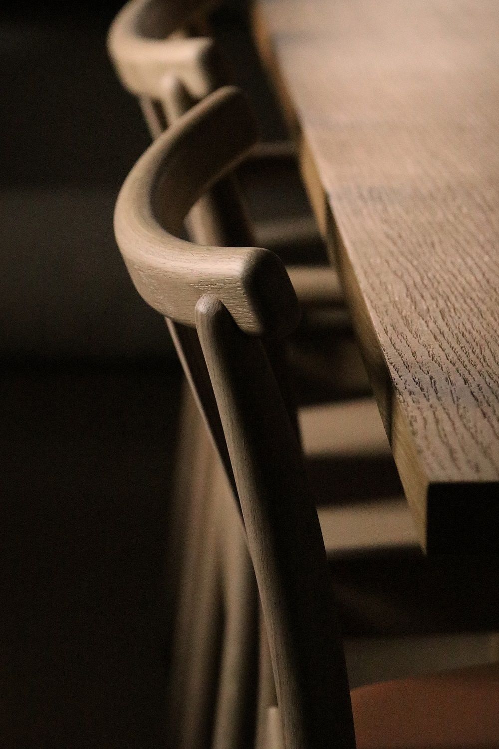 Detailaufnahme des Audo Copenhagen Merkur Dining Chair Stuhls mit Armlehne aus hellem Holz.