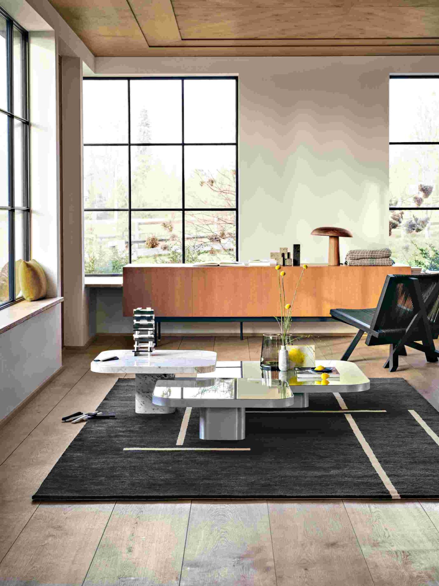 Moderner Wohnraum mit ClassiCon Bow Coffee Table, Marmor-Couchtisch und Designermöbeln auf einem dunklen Teppich.