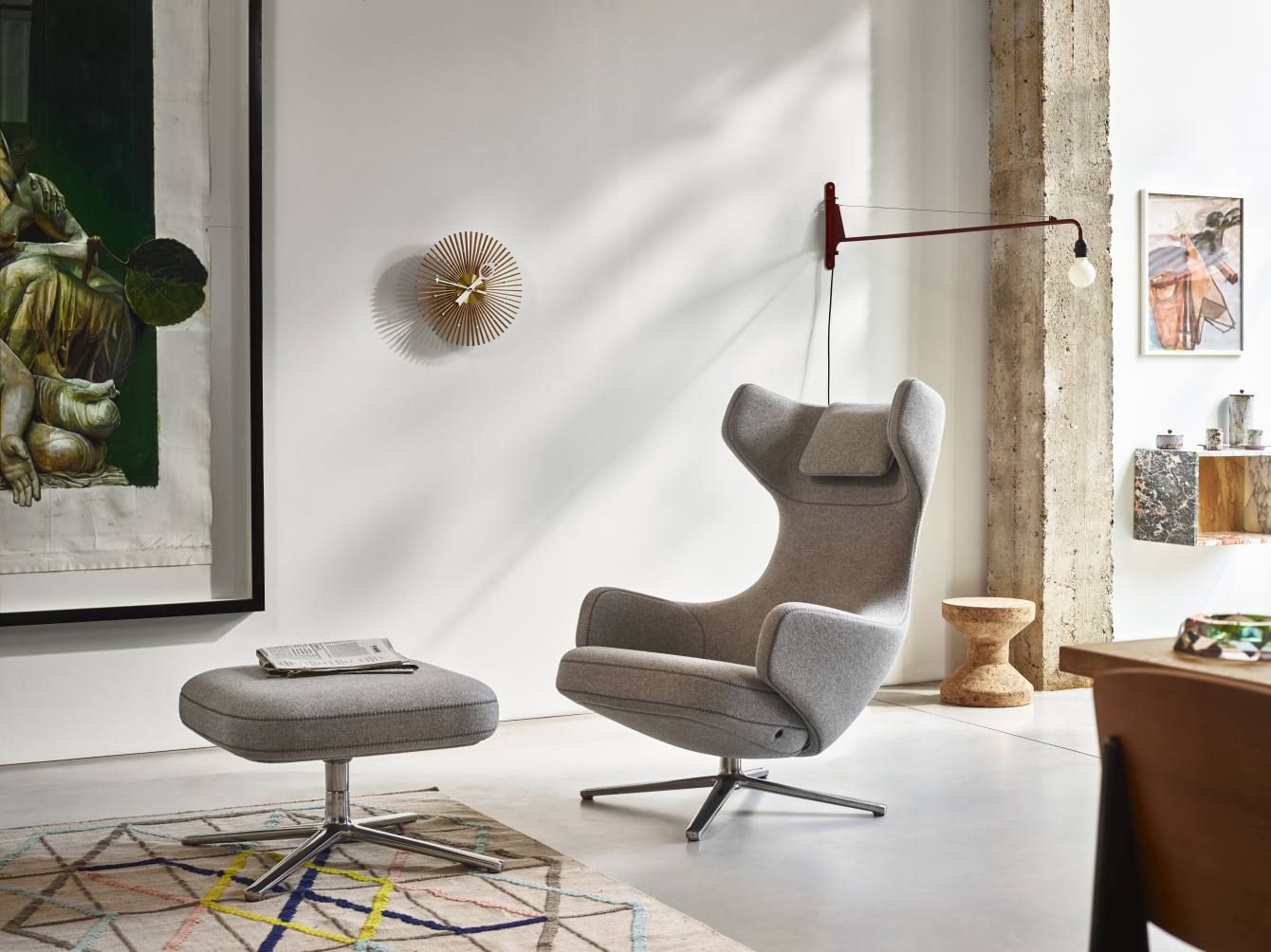 Wohnzimmer-Szene mit Vitra Popsicle Clock Wanduhr, grauem Sessel und Hocker auf einem Teppich.