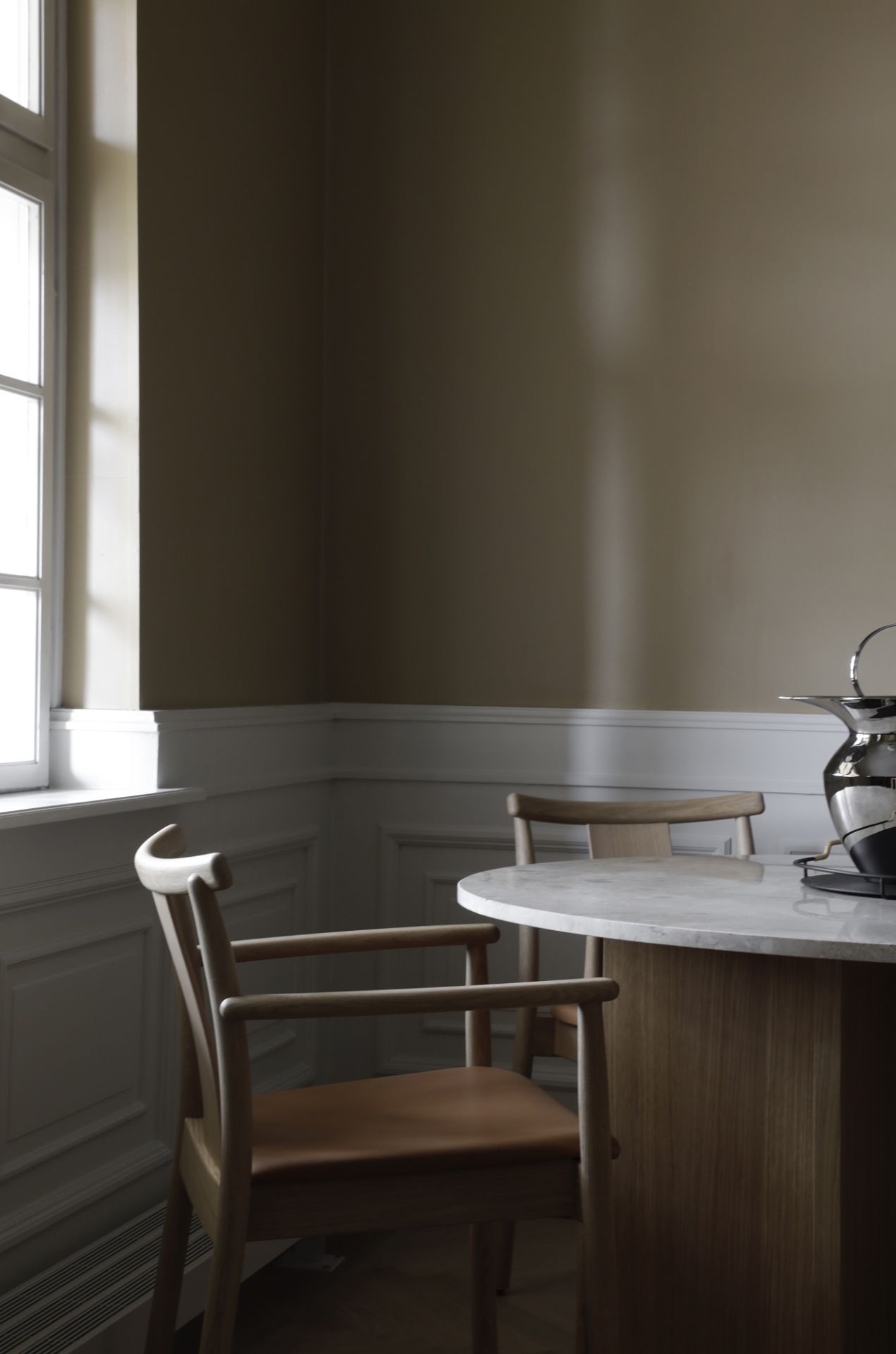 Merkur Dining Chair Stuhl mit Armlehnen von Audo Copenhagen am Esstisch, helle Holzstruktur und Ledersitz.