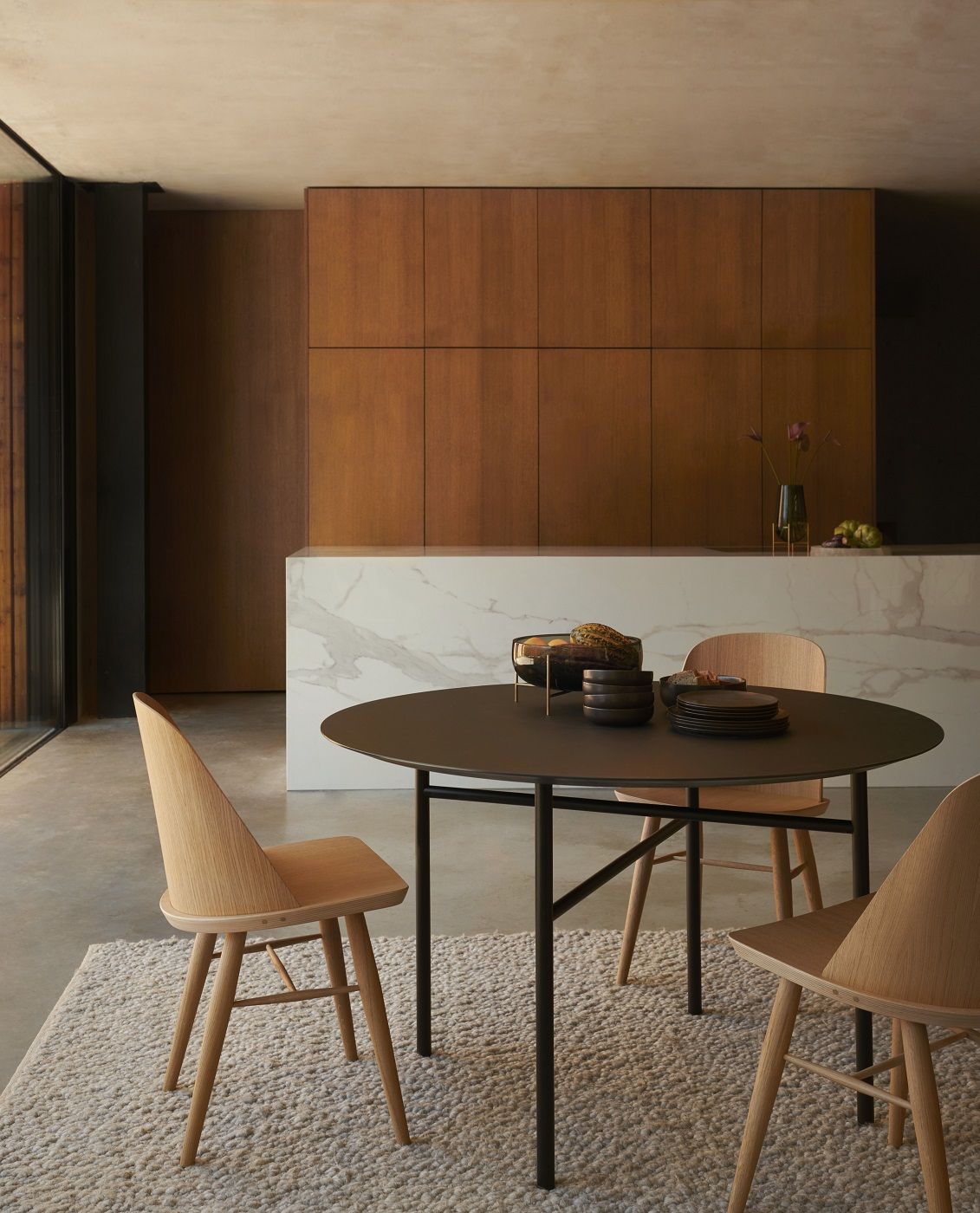 Audo Copenhagen Gravel Rug Teppich in einem Esszimmer mit Esstisch und Holzstühlen.