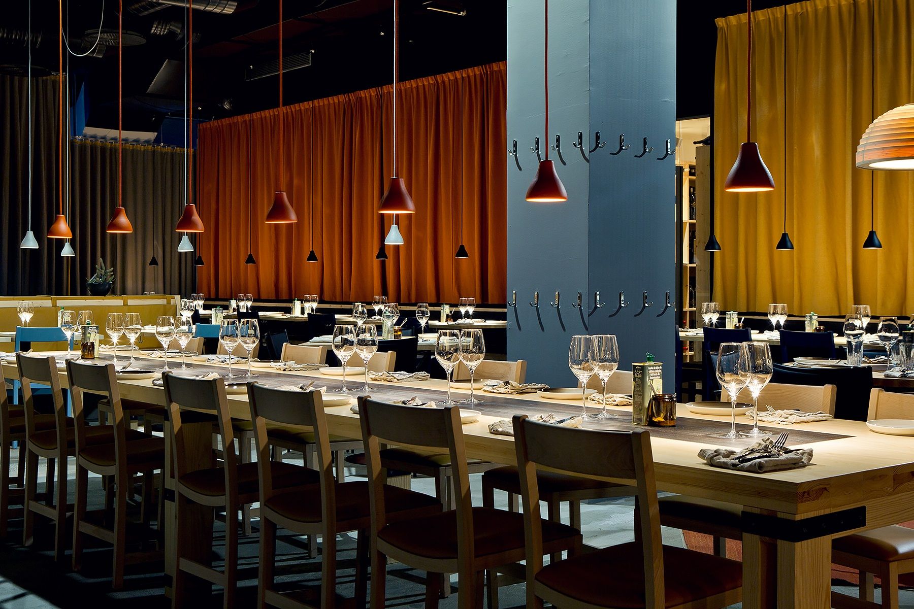 Innenaufnahme eines Restaurants mit gedecktem Tisch und mehreren w131 Bell Pendelleuchten von wästberg in Rot und Weiß.