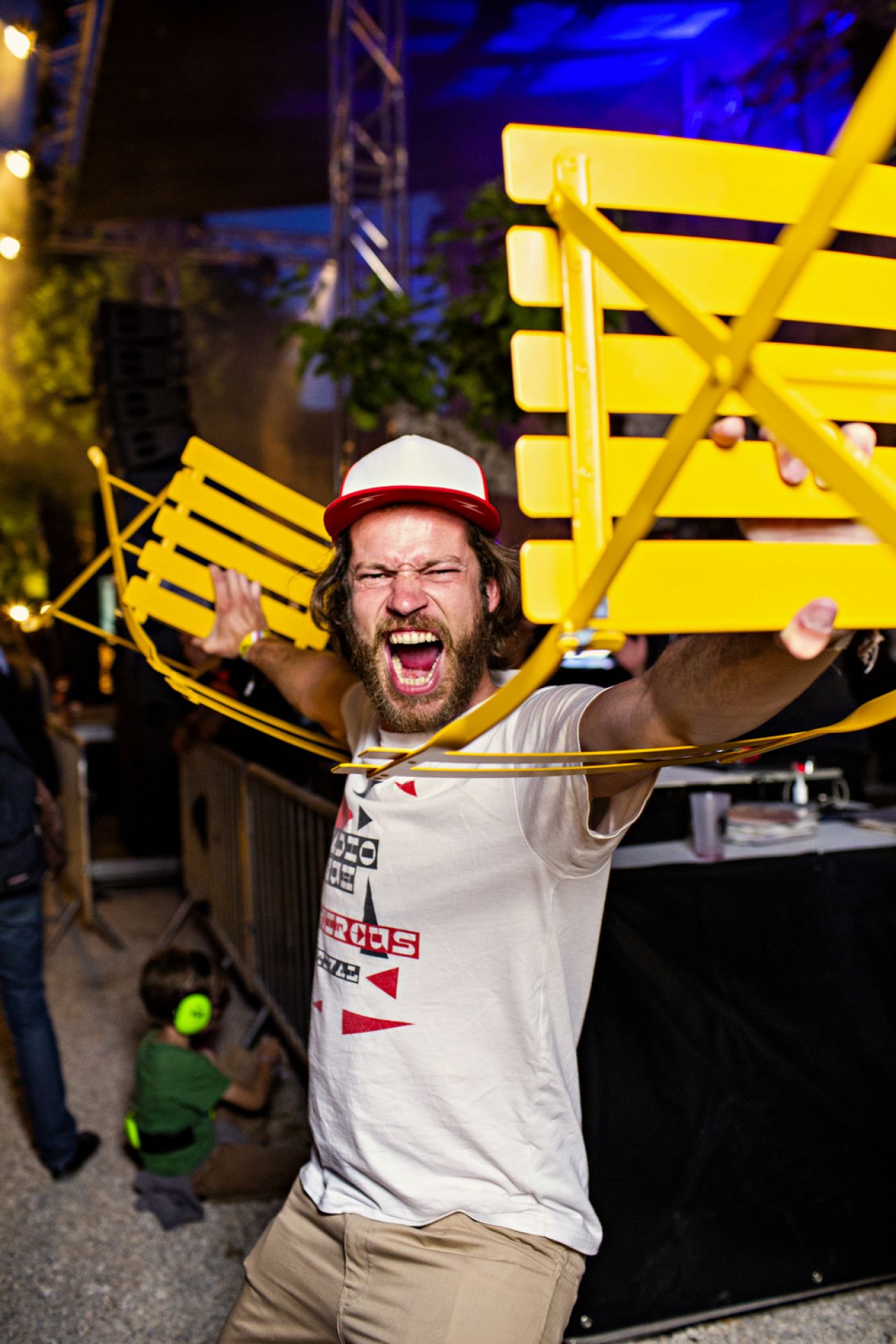 Mann hält gelben Bistro Outdoor Metallstuhl von Fermob hoch, schreit und feiert auf einer Party.