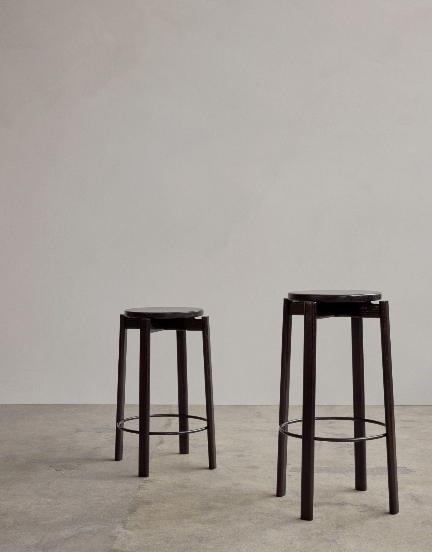 Zwei Audo Copenhagen Passage Bar Stools aus dunklem Holz mit runden Sitzen und Fußstützen.