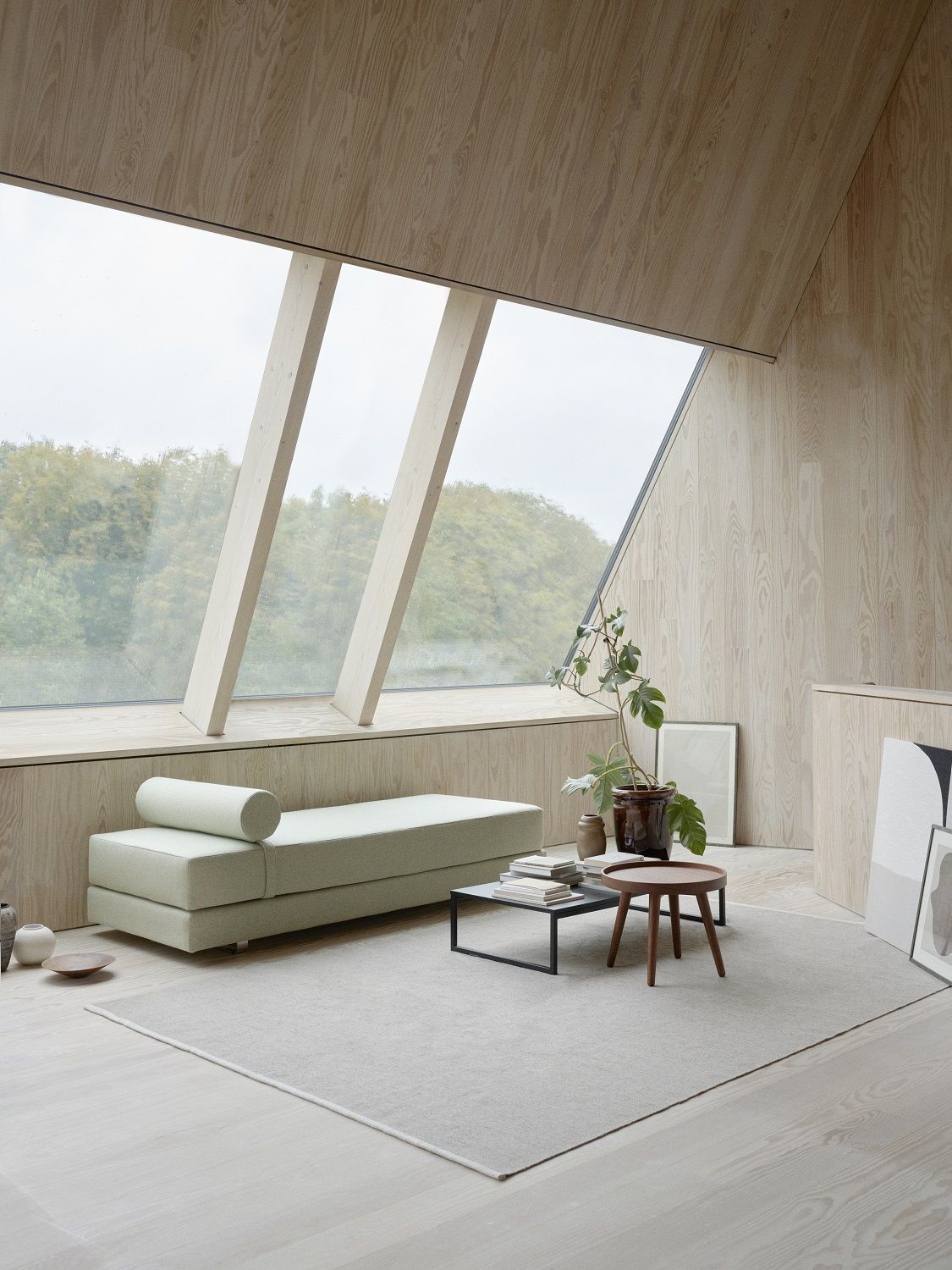 Helles Wohnzimmer mit Lubi Daybed Schlafsofa in Mintgrün, minimalistisches Design mit großem Fenster und Holzwänden.