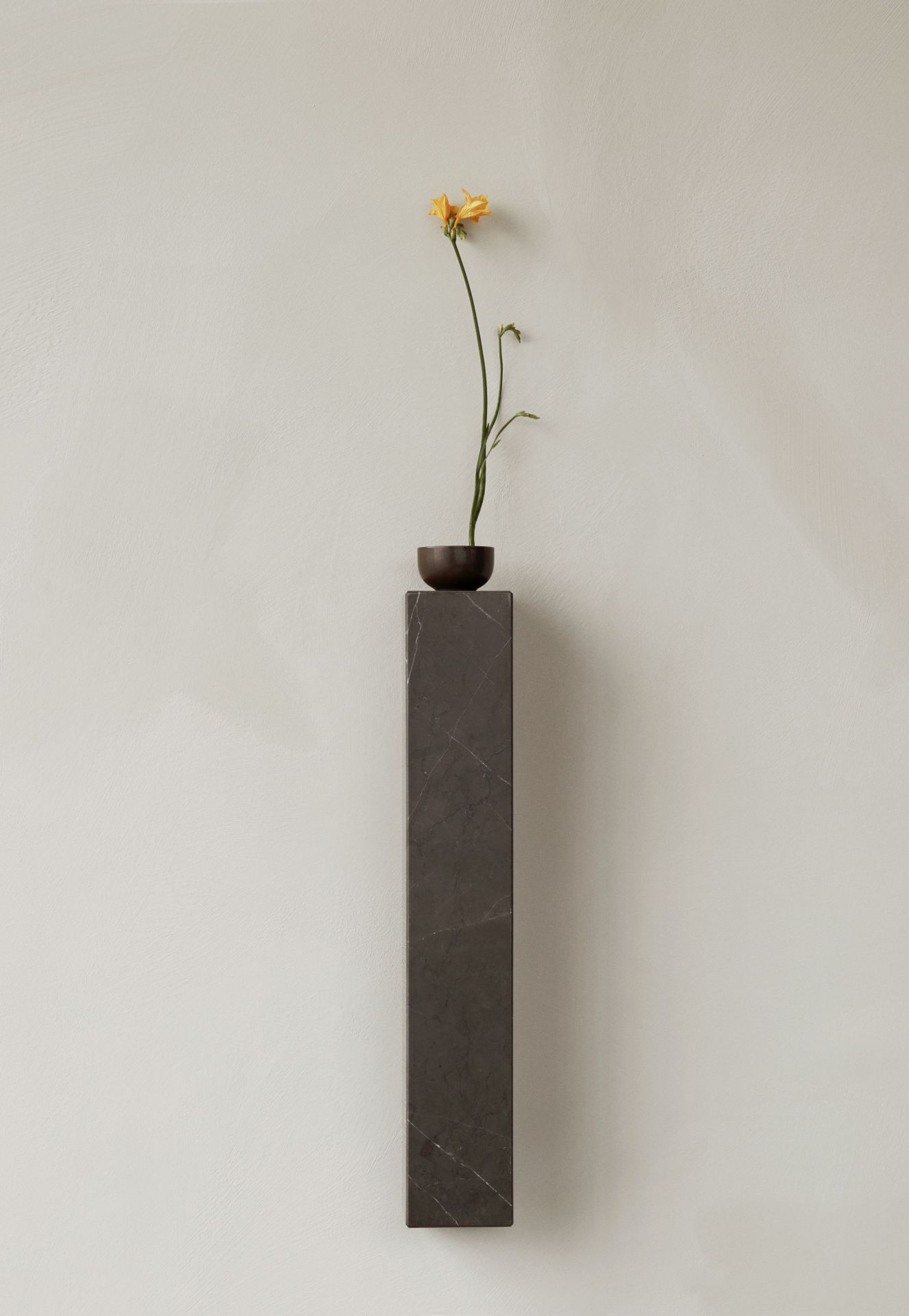 Audo Copenhagen Plinth Shelf Regal aus Marmor mit gelber Blume in dunkler Vase.