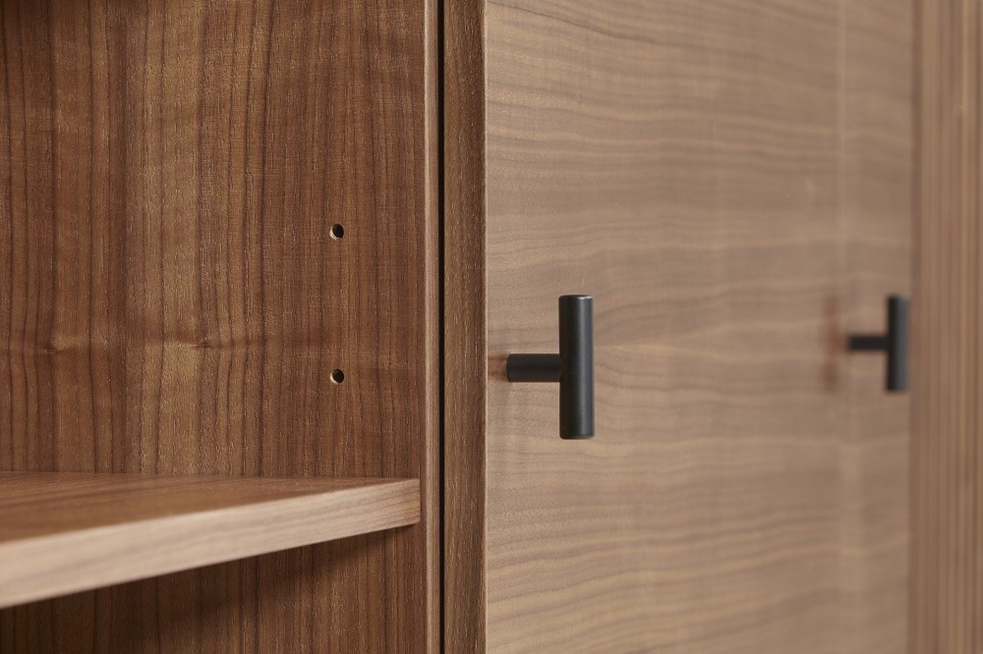 Detailaufnahme: Array Sideboard aus Walnuss von Woud mit schwarzen Griffen und Regalböden.