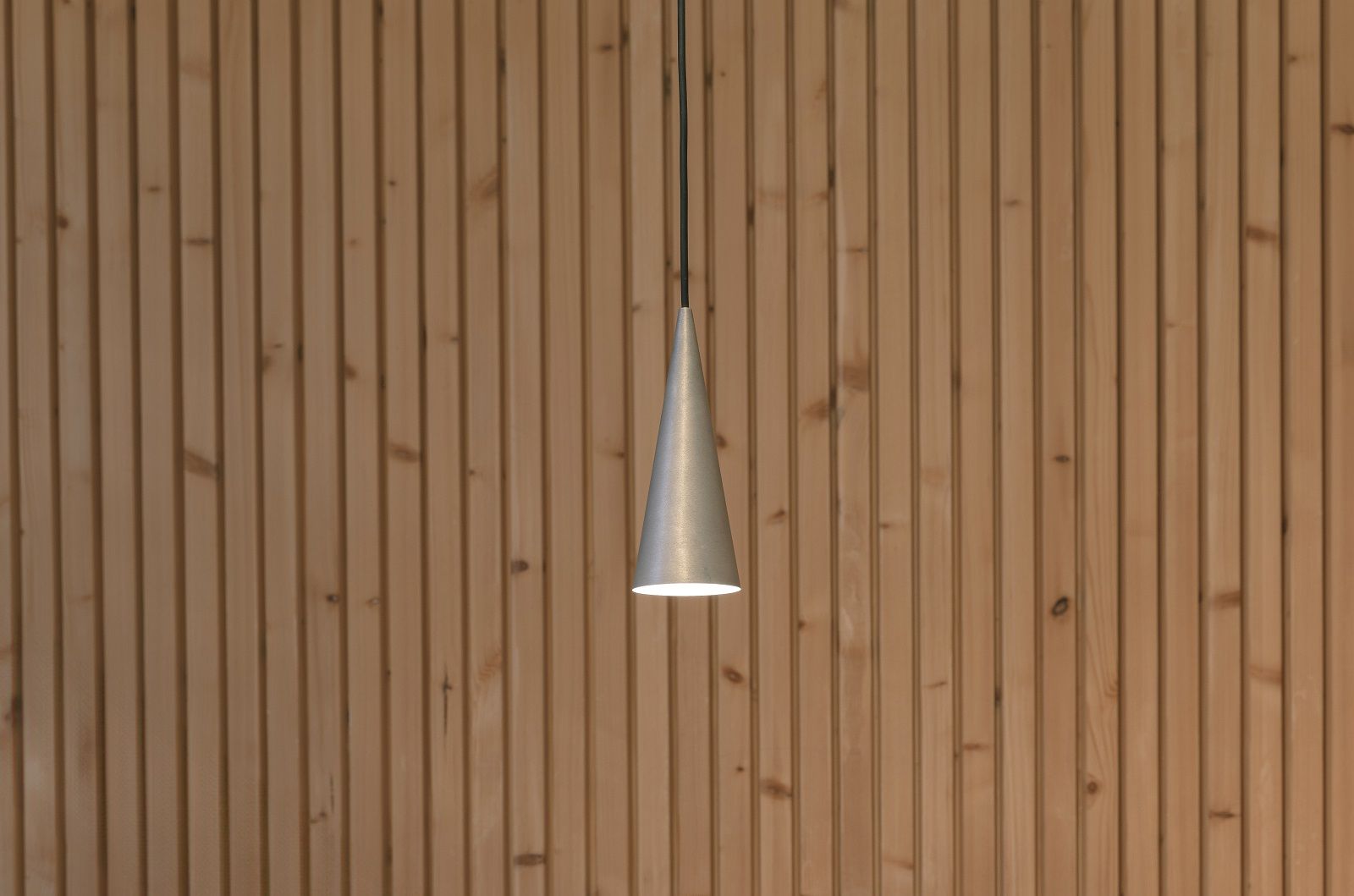 w201 S1 Pendelleuchte von wästberg, Kegelförmige Hängelampe aus Aluminium vor einer Holzwand.