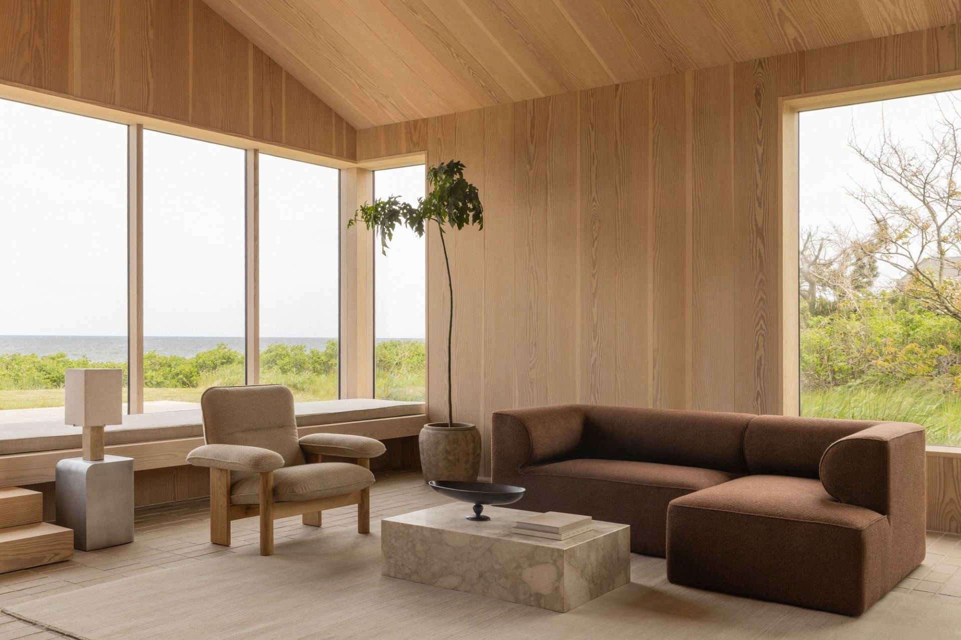 Helles Wohnzimmer mit Audo Copenhagen Volume Side Table, Sessel, Sofa und großem Fenster mit Meerblick.