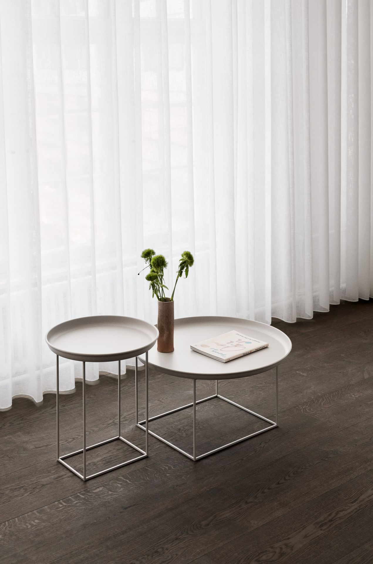 Norr11 Duke Beistelltisch Set: Kleiner, grauer runder Tisch mit Blumen und Buch vor Fenster.