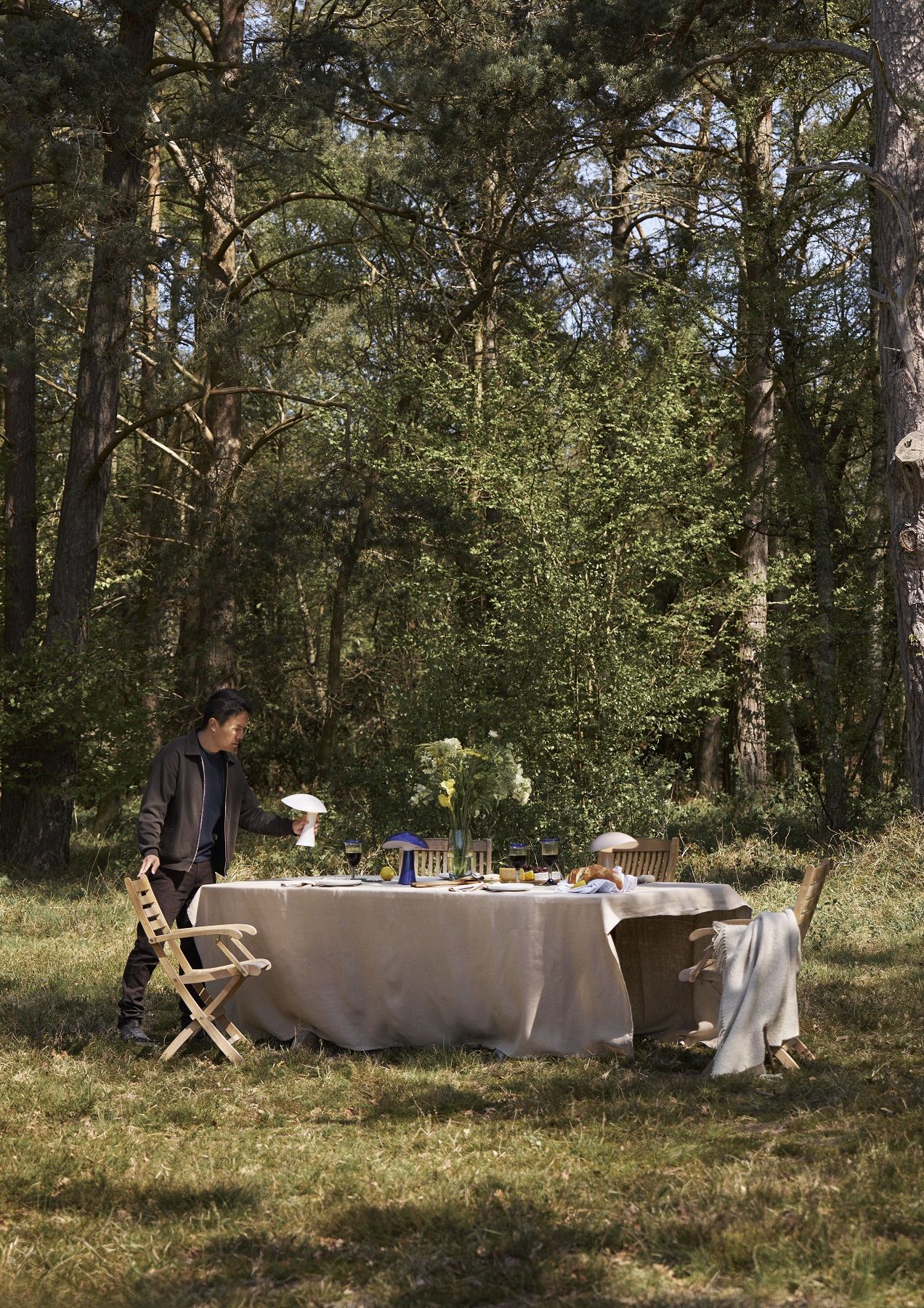 Rumee Akkuleuchte von Louis Poulsen auf gedecktem Tisch im Freien, stimmungsvolle Beleuchtung für Outdoor-Dinner.