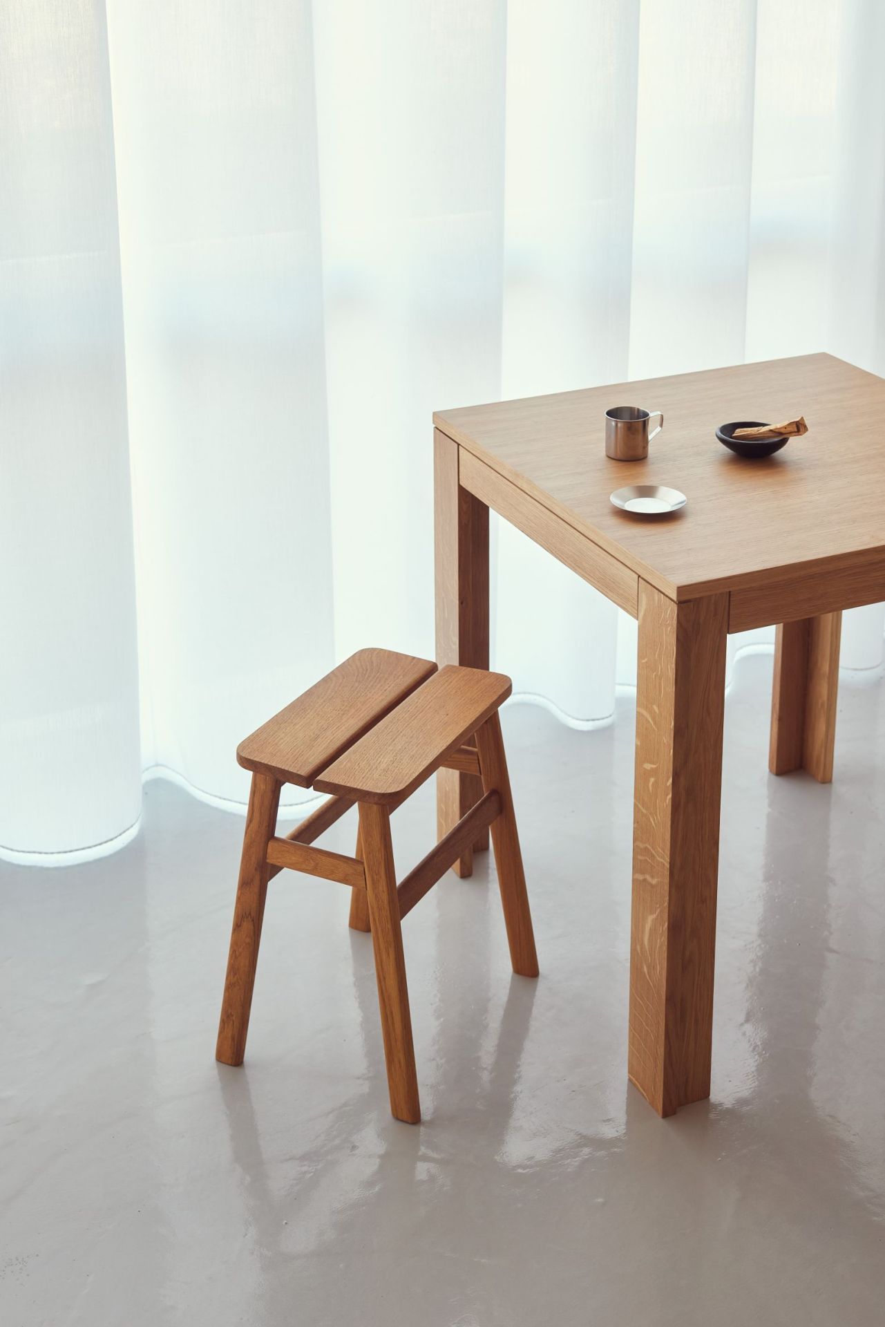 Form & Refine Element Tisch 70x70 aus Eiche mit Hocker und Accessoires vor hellem Vorhang.