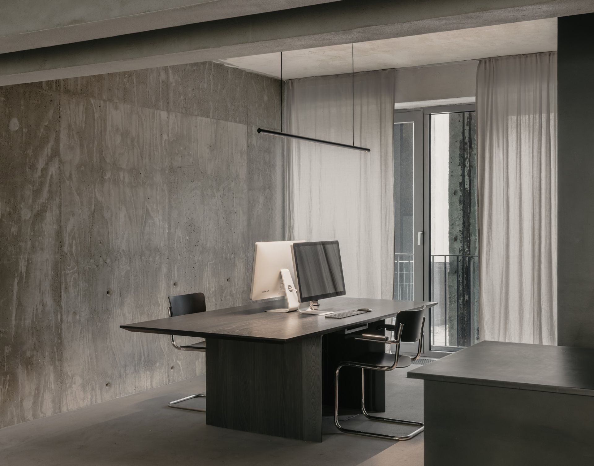Moderne Büroeinrichtung mit wästberg w181 S2 Linier Pro Pendelleuchte über dunklem Holztisch und zwei Computern.