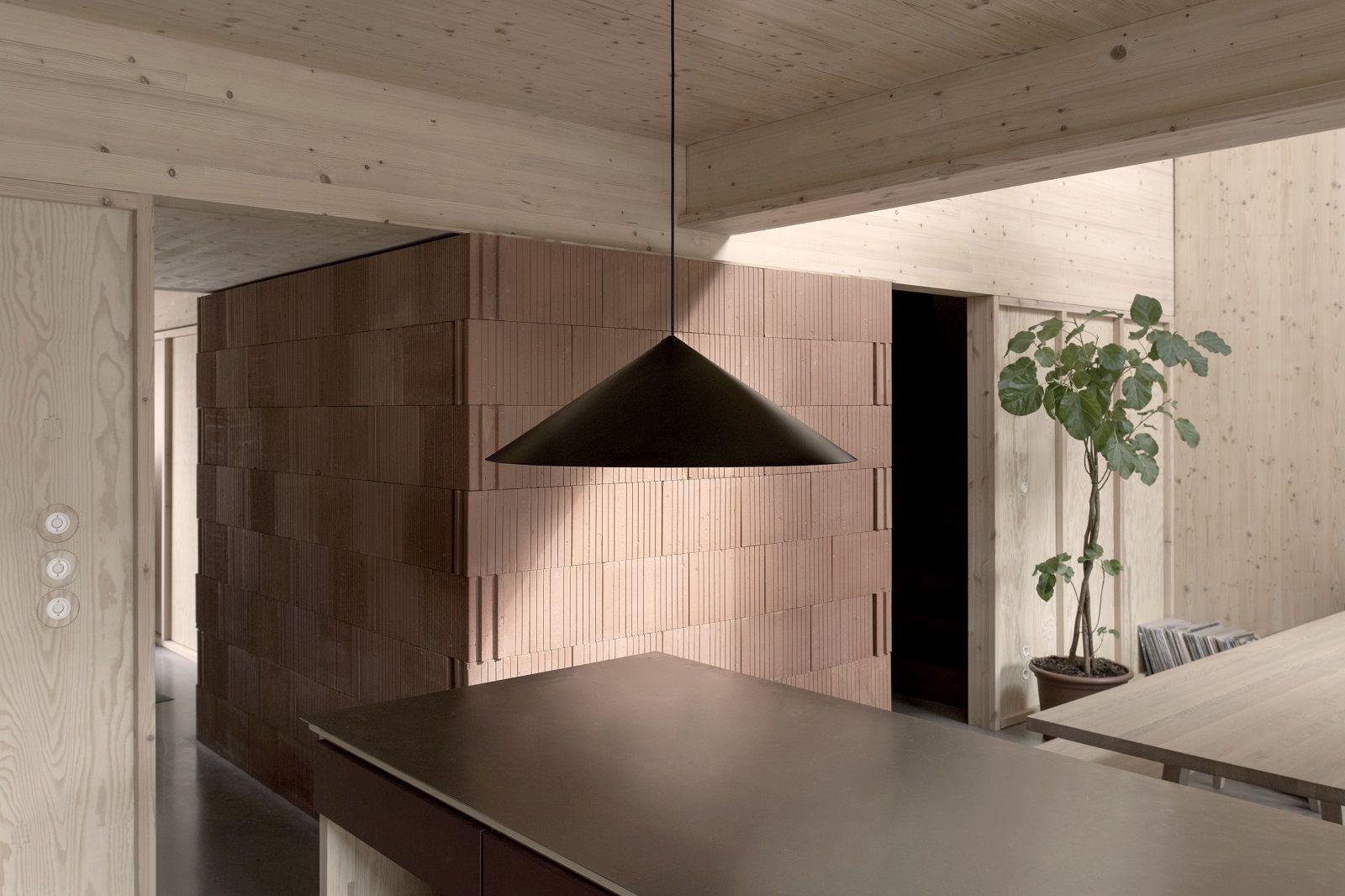 w221 S3 Medium Pendelleuchte von wästberg in modernem Interieur mit Holzwänden und Backsteinmauer.