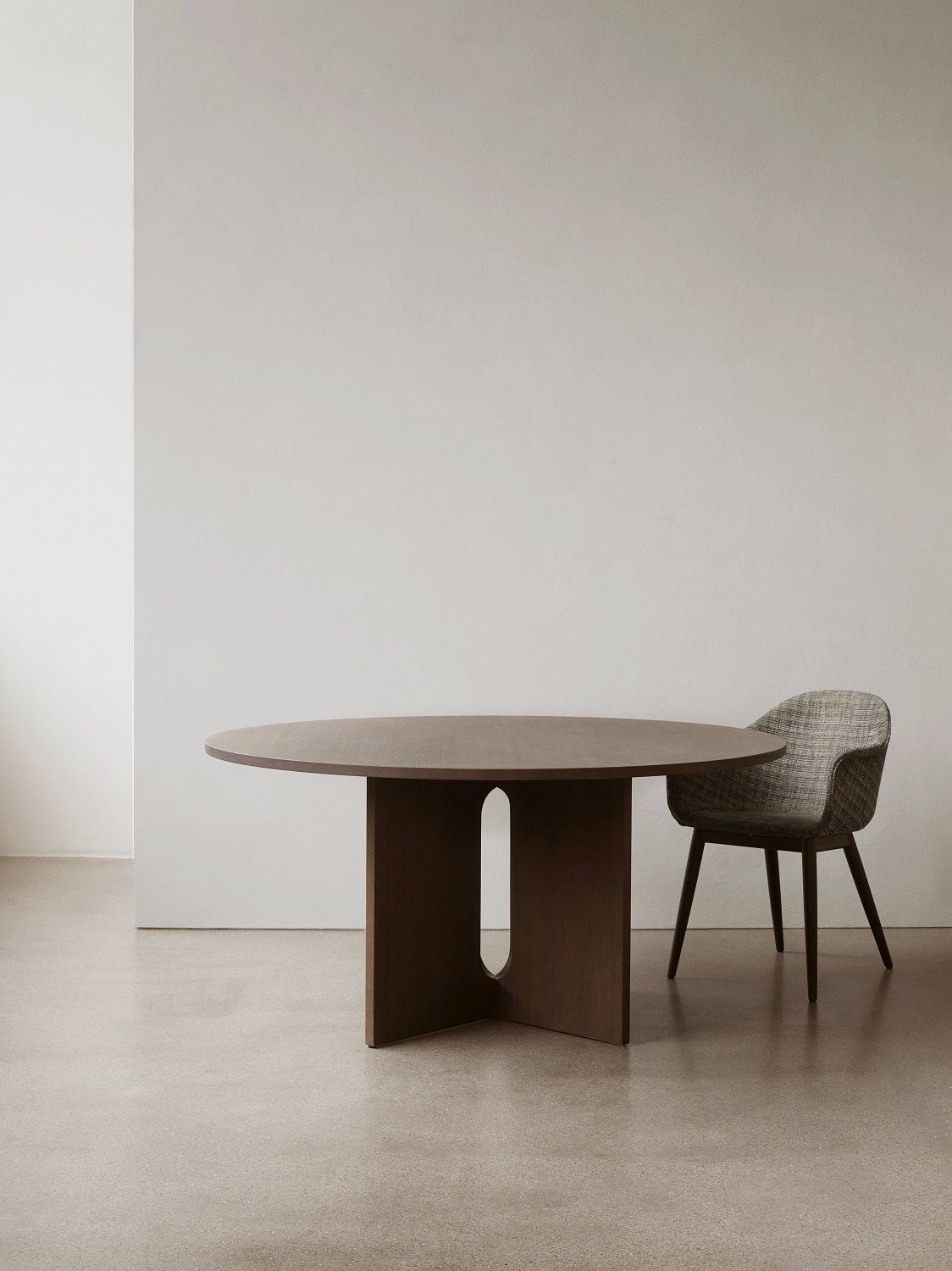Audo Copenhagen Harbour Dining Chair Stuhl neben einem runden Esstisch aus dunklem Holz.
