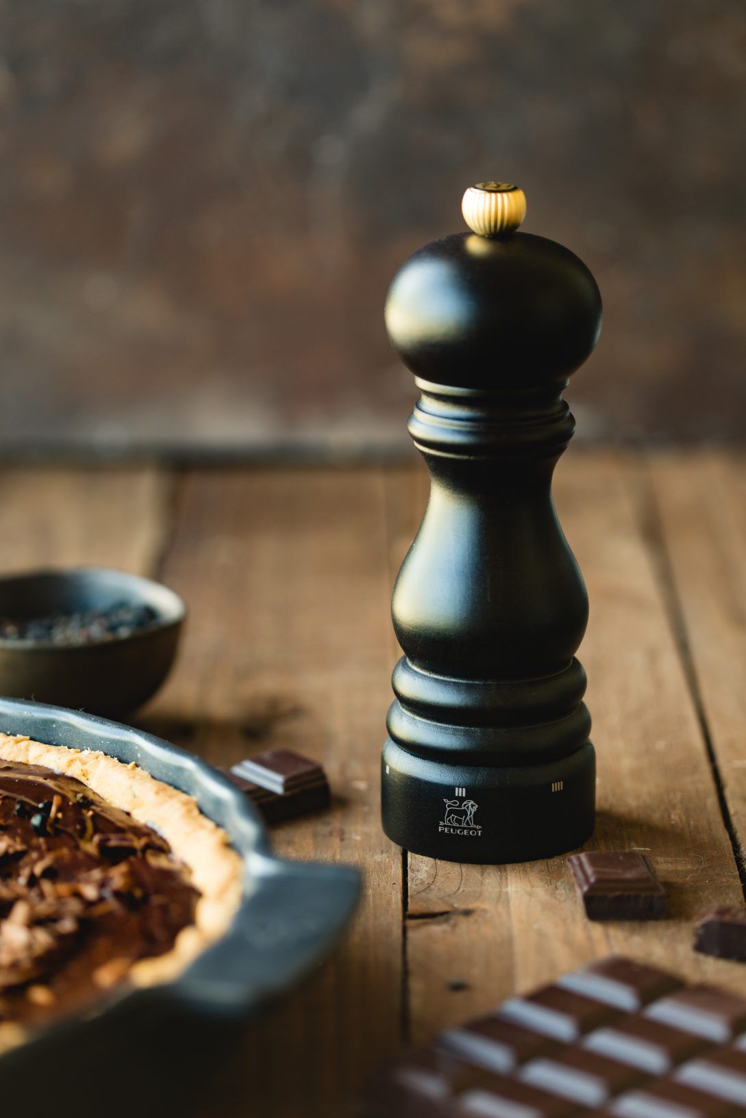 Peugeot Paris Pfeffermühle 18 cm Schokolade neben Schokoladenkuchen und Schokoladenstücken auf einem Holztisch.