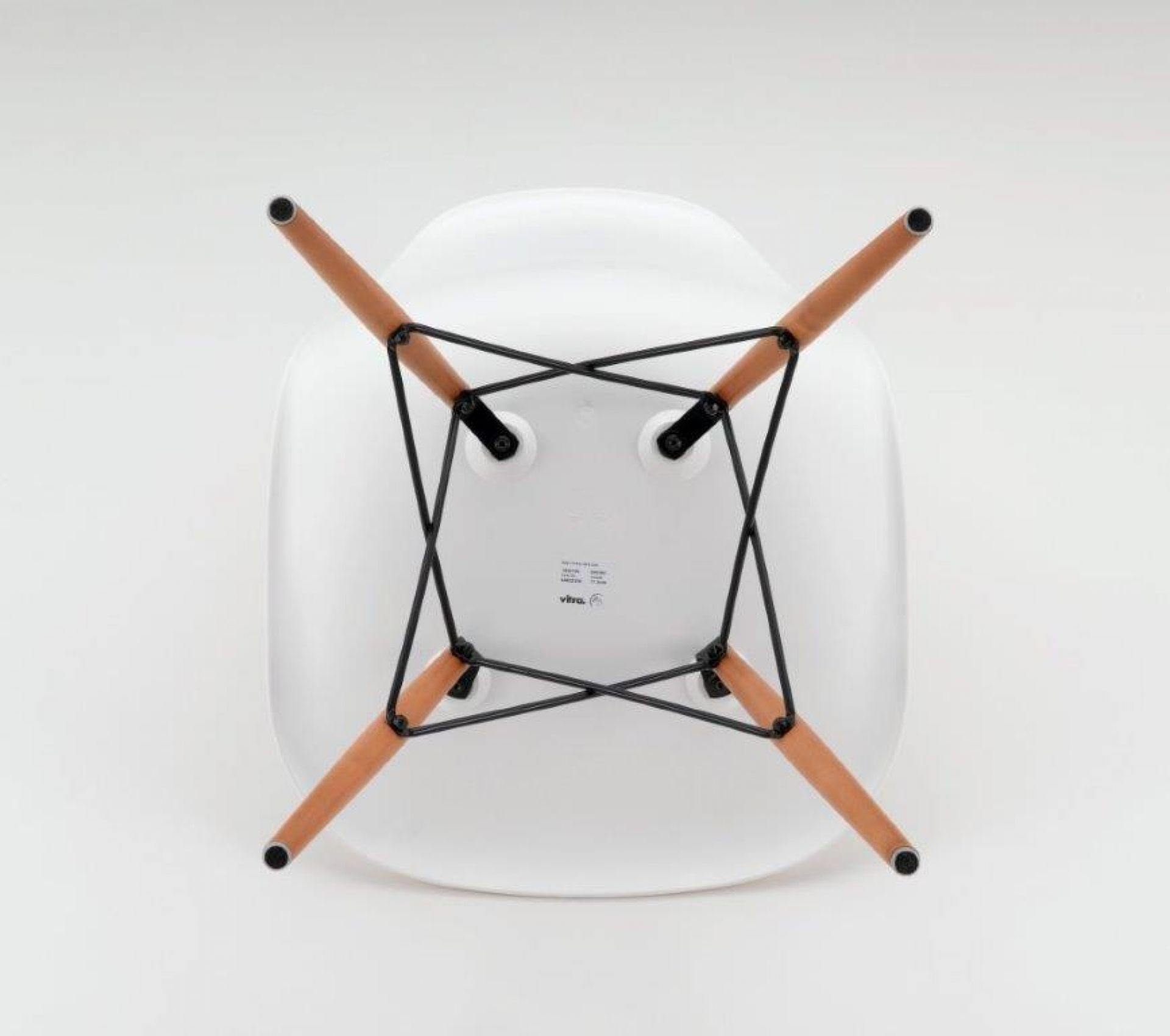 Detailaufnahme der Unterseite eines weißen Eames Plastic Side Chair DSW Stuhls von Vitra mit Holzbeinen.