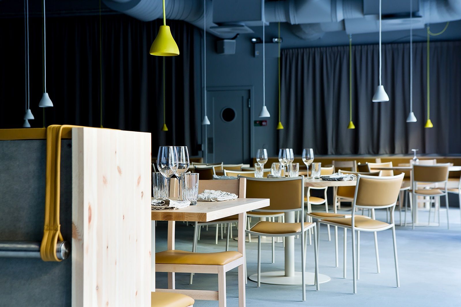Innenaufnahme eines Restaurants mit Tischen, Stühlen und mehreren w131 Bell Pendelleuchten von wästberg in Gelb und Weiß.