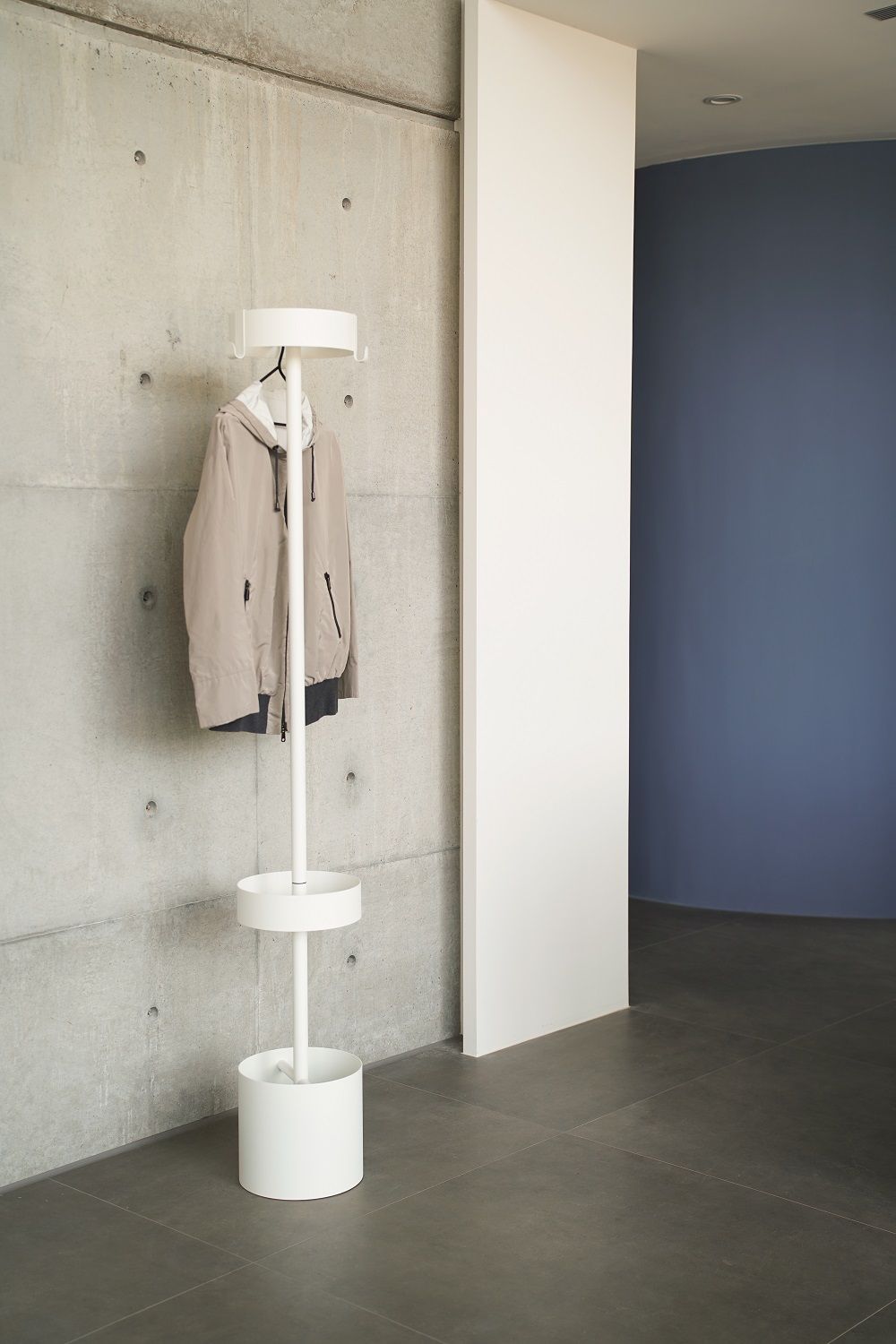 Weißer Oolo Garderobenständer Mox mit Jacke vor Betonwand, minimalistisches Design für Flur und Eingangsbereich.