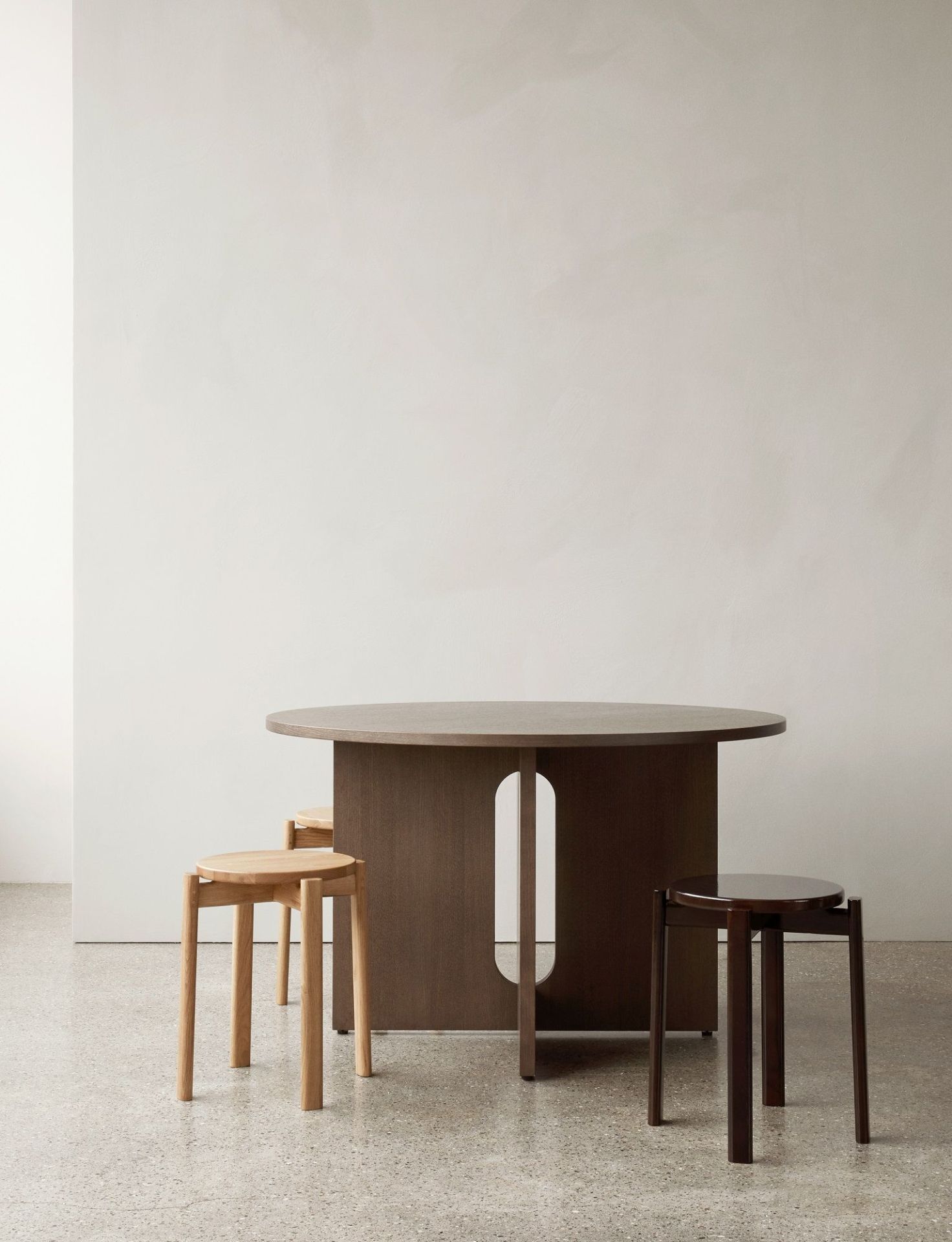 Audo Copenhagen Passage Stool Hocker aus Holz in verschiedenen Farben unter einem Holztisch.