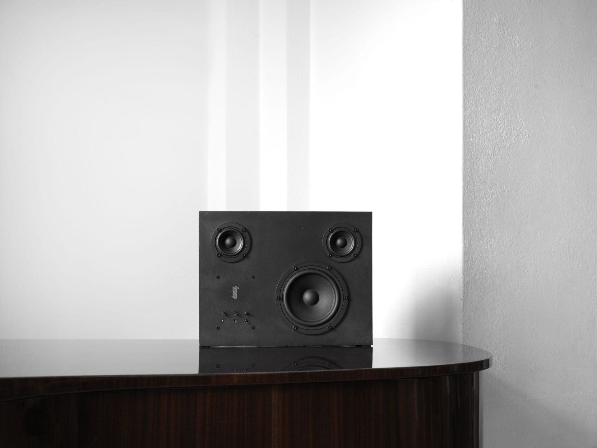 Schwarzer Stahl Lautsprecher mit transparentem Klang auf dunklem Holzmöbel, minimalistisches Design für Hi-Fi-Enthusiasten.