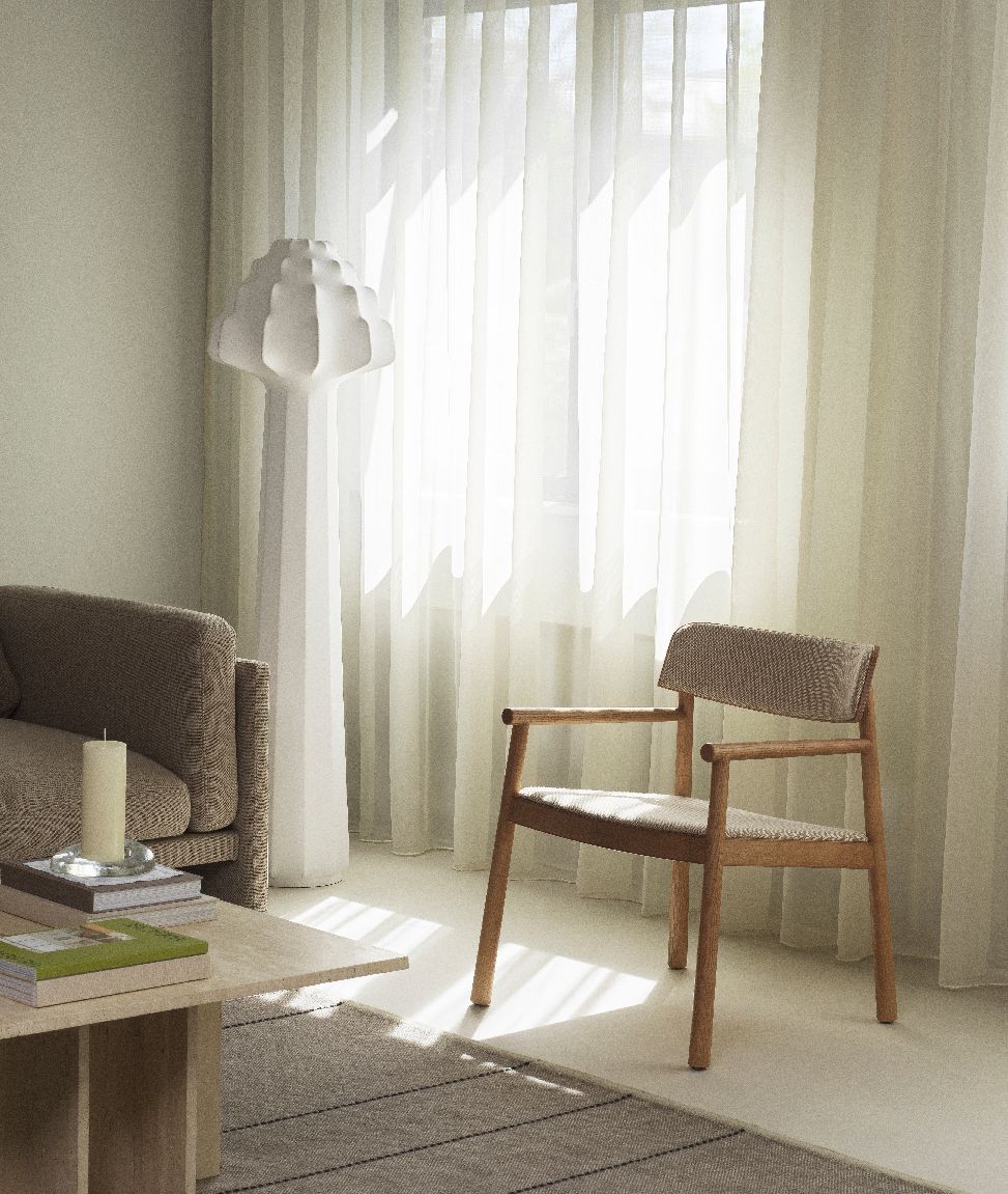 Helle Wohnzimmer-Szene mit Normann Copenhagen Phantom Stehleuchte, Sessel und Sofa bei Tageslicht.