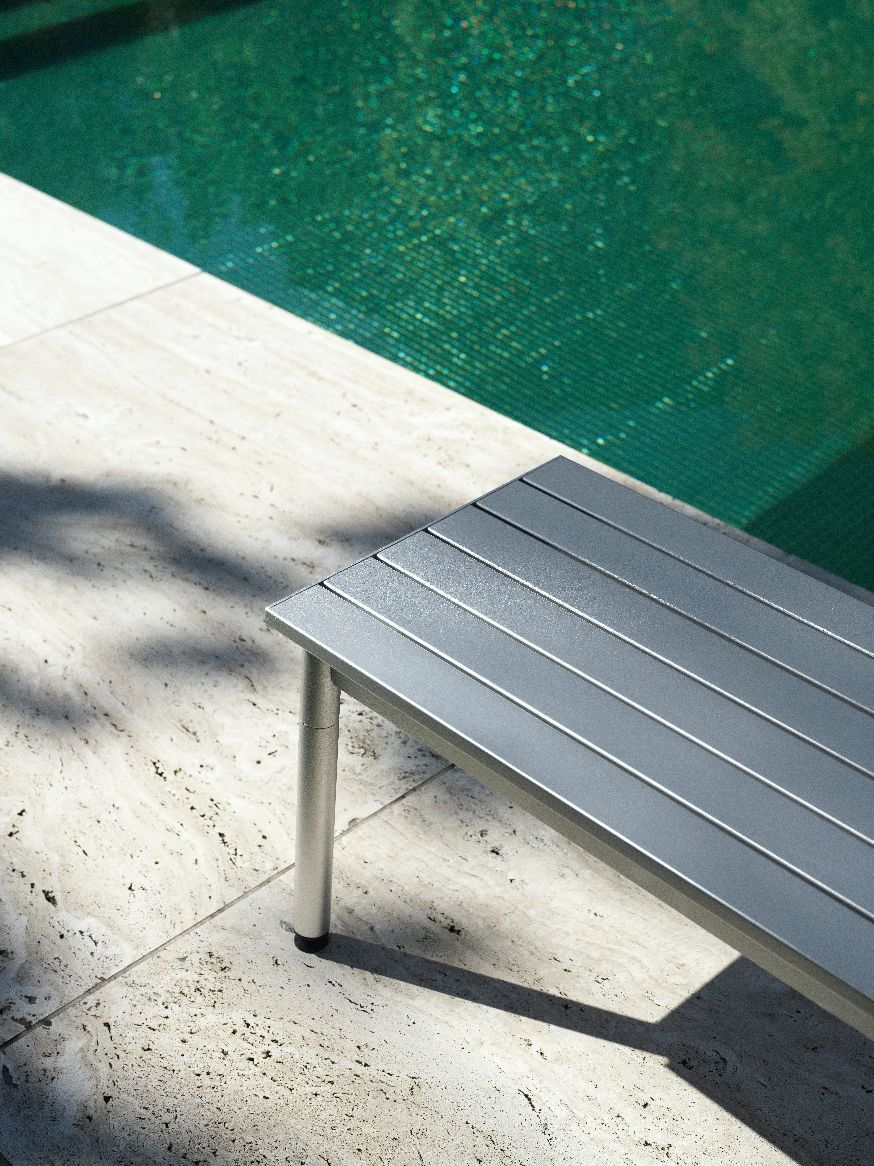 Nahaufnahme der grauen Normann Copenhagen Ex Bank Outdoor neben einem Pool auf Steinfliesen.
